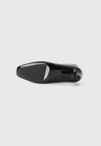 Sole di scarpa in pelle nera con una finitura liscia, punta leggermente appuntita e un motivo di battistrada minimale. Presenta un dettaglio di marca sul lato.
