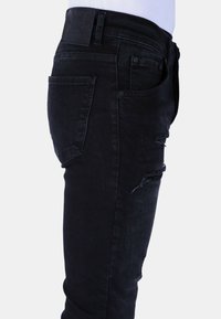 Zwarte denim jeans met een slim fit, voorzien van distressed accenten op de dij en een vlakke achterzak. De tailleband heeft een leren merklabel.