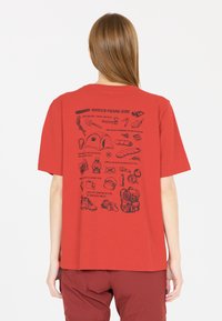 Punainen lyhythihainen t-paita, jossa on mustia kuvastoja retkeilyvarusteista selkäpuolella, mukaan lukien teltta, taskulamppu ja reppu.