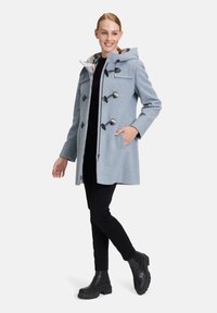 Lichtblauwe duffelcoat met capuchon, toggle sluitingen, twee zakken en een geruite voering. Draagt over zwarte broek en laarzen.