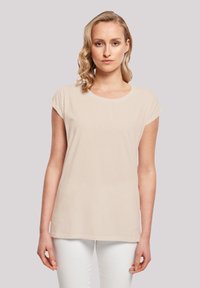 Beige short-sleeve t-shirt made from soft fabric, featuring a round neckline and a relaxed fit, worn with white pants.