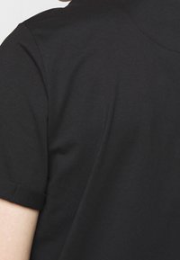 Černé polo tričko s krátkým rukávem, vyrobené z jemného materiálu, s klasickým límečkem a srolovanými manžetami. Jednoduchý, čistý design.