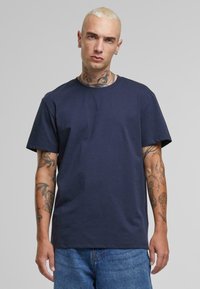 Tricou din bumbac de culoare albastru marin, cu mâneci scurte, gât rotund și croială lejeră. Are tatuaje vizibile pe brațe și o fustă din denim cu tăietură dreaptă.