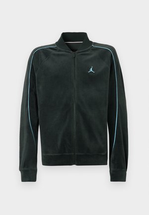 Crna jakna na zip od mekanog materijala, s svijetlosmešnim obrubom duž ramena i malim plavim logom na lijevoj strani prsnog koša.