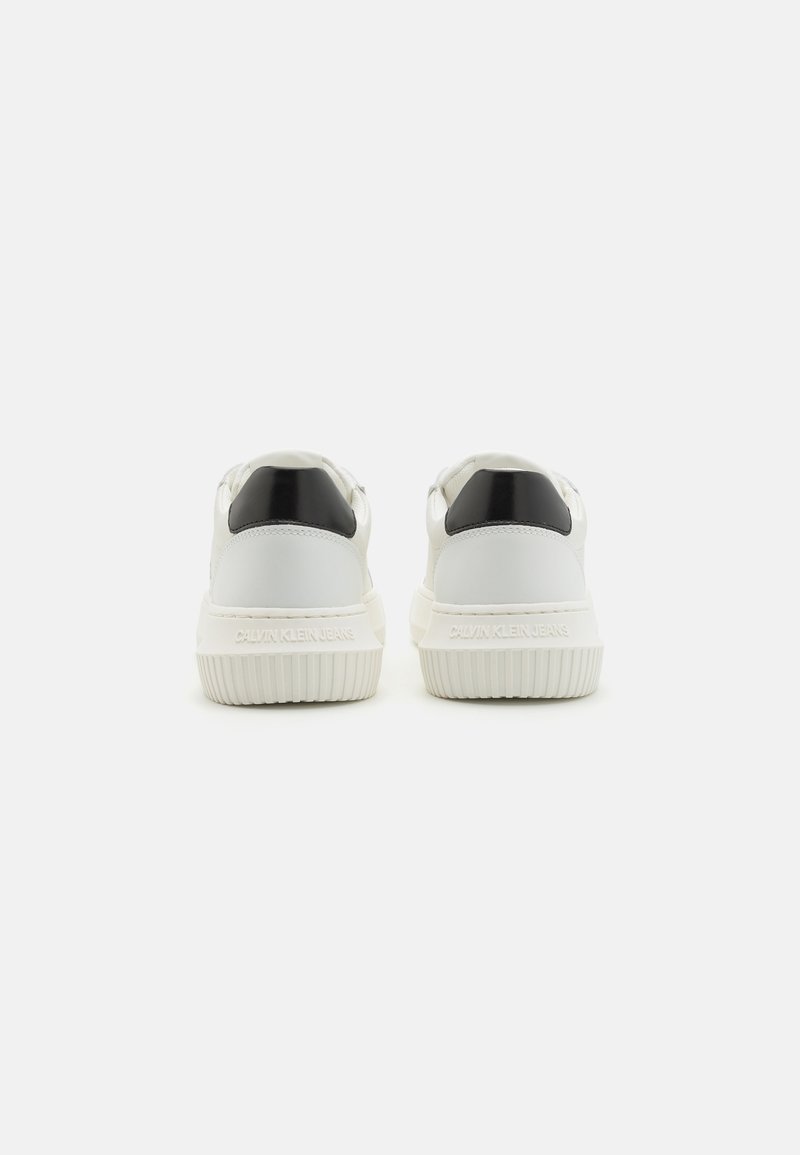 Weiße Sneaker mit einem glatten Lederoberteil und einem schwarzen Akzent an der Ferse, einer strukturierten Gummisohle und geprägt Branding.