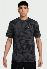 Camiseta atlética negra con un patrón abstracto texturizado, cuello redondo, mangas cortas y un logo blanco de Nike en el lado izquierdo del pecho.