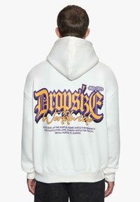Sweatshirt à capuche blanc avec un texte graphique audacieux en violet et noir au dos. Le matériau semble doux, avec des poignets et un ourlet côtes.