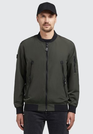Olívazöld bomber dzseki cipzáros elülső résszel és oldalsó zsebekkel. Ribbed mandzsetták és derékpánt. Készült sima, könnyű anyagból. Fekete sapka.