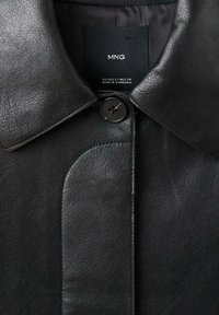 Czarna skórzana kurtka z zaokrąglonym kołnierzem, pojedynczym zapięciem na guzik oraz gładką fakturą z delikatnym wzorem ziarnistości. Wewnątrz widoczna metka.