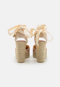 Espadrillas con tacco alto in tessuto intrecciato beige, con tallone aperto e dettagli in pelle rosa. Presentano lacci in raso e una zeppa in juta texturizzata.