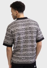 Knit short-sleeve shirt in black and white, featuring horizontal patterned stripes and a black collar. Textured fabric adds depth.