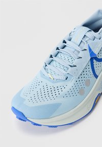 Hellblaues Laufschuhmodell mit Obermaterial aus Mesh, Perforationen für Atmungsaktivität, blauen Akzenten und einer gepolsterten Sohle mit strukturiertem Profil.