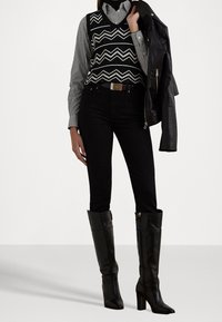 Czarne wysokie buty na obcasie ze spiczastym noskiem, zestawione z czarnymi dżinsami, czarno-białą kamizelką w wzory na koszuli w paski oraz skórzaną kurtką.