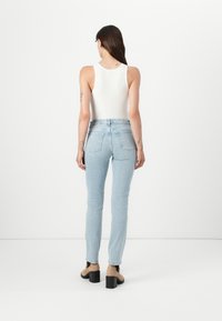 Jean skinny taille haute bleu clair avec une texture en denim doux, présentant des poches arrière, associés à un top sans manches blanc et des talons noirs.
