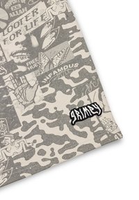 Canvas stof met een grijs camouflagepatroon, afgewisseld met verschillende grafische prints en een zwart "Grimy" logo patch.