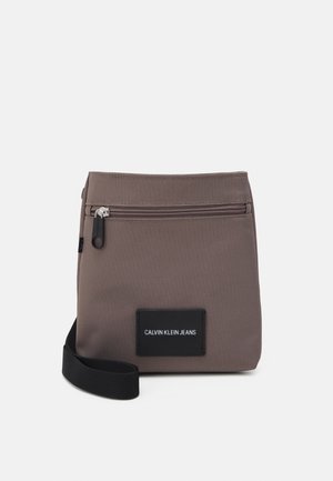 Compact brown crossbody bag with front zipper pocket, black adjustable strap, and "Calvin Klein Jeans" label on front.