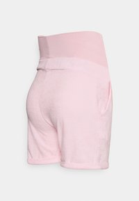 Calções cor-de-rosa, macios, com uma cintura larga, apresentando dois bolsos laterais e com as bainhas dobradas. A textura aparenta ser fofa e leve.