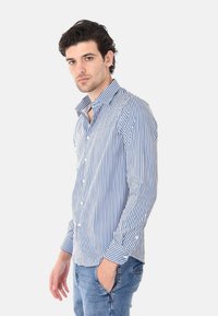 Camicia a righe blu e bianche con colletto standard, maniche lunghe e vestibilità slim, abbinata a jeans blu chiaro.