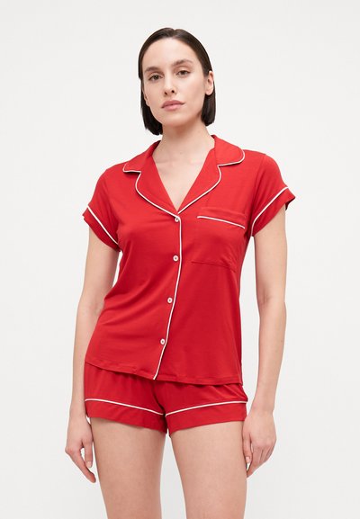 Red pajama set featuring short-sleeved top with a pocket, white piping, and matching shorts, made from soft, stretchable fabric.