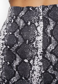 Primo piano di un tessuto a stampa serpente bianco e nero su un indumento a vita alta indossato da una persona.