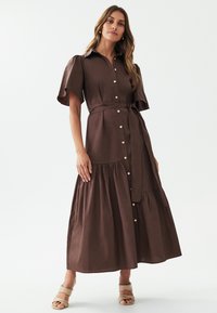 Abito marrone con bottoni, maniche corte a soffietto, vita con cintura e gonna a strati. Tessuto liscio con un design casual e fluido.