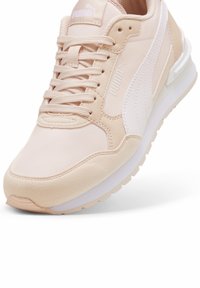 Baskets Puma beige et blanches avec semelle texturée, devant à lacets, et logo Puma sur le côté et la languette.