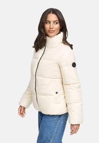 Giacca puffer crema con colletto alto, cerniera nera e bottoni; presenta un design trapuntato e tasche laterali. Texture morbida e liscia.