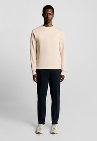 Licht beige sweatshirt met lange mouwen, ronde hals en subtiele logodetail. Gekocht met donkerblauwe broeken en beige sneakers.