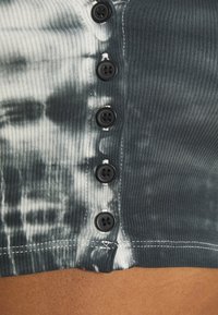 Schwarz-weißer Batik-Top im Cropped-Stil mit gerippter Textur, ausgestattet mit sechs schwarzen Knöpfen auf der Vorderseite und weißem Stich am Saum.