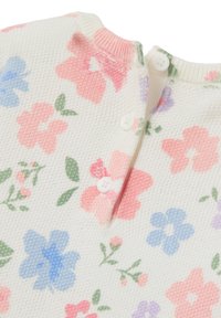 Top en tricot floral crème avec des fleurs roses, bleues et vertes. Dispose d'une patte de boutonnage et d'un col ribbé. Tissu texturé.