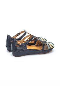 Sandalias de cuero negro con diseño recortado, con acentos de cuero marrón y detalles de costura. Suela blanda y plana con interior ligero.