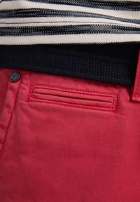 Rode katoenen broek met een gemêleerde tailleband, voorzien van een zijzak met horizontale stiksels en een donkere knoopaccent.