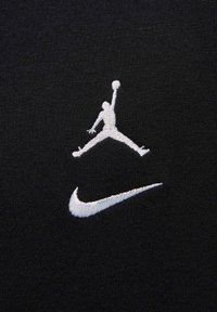 Tessuto nero con logo Jumpman ricamato in bianco e swoosh Nike, che mette in evidenza una texture liscia e un design distintivo.