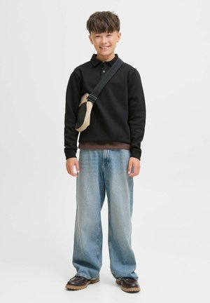 Schwarzes Langarm-Polo, hellbraunes Unterhemd, weite blaue Jeans, braune Stiefel und eine beige Umhängetasche mit Netzdetail.
