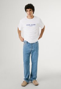White cotton t-shirt featuring blue "PEPE JEANS LONDON" text. Paired with light blue denim jeans and beige slip-on shoes. Simple design.
