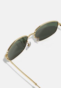 Lunettes de soleil en métal doré avec des verres vert foncé, monture ovale slim, plaquettes de nez ajustables et branches droites pour un design minimaliste.