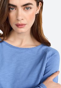 Blue long-sleeve shirt with a round neckline, featuring a soft, textured fabric and subtle stitching details at the collar.
