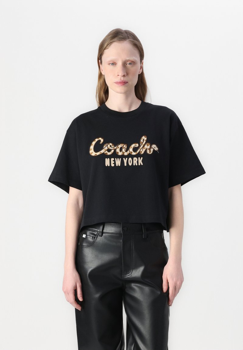 Juodas trumpas marškinėliai iš medvilnės su spausdintu „Coach New York“ logotipu kontrastinga smėlio spalvos ir gyvatės odos raštu.