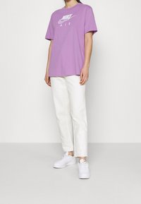 Fialové bavlněné tričko s bílým logem "Nike Air", kombinované s bílými kalhotami rovného střihu a bílými teniskami. Jednoduchý, volnočasový outfit.