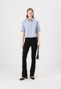 Korte mouw shirt met blauwe en witte verticale strepen, gecombineerd met zwarte uitlopende broek en zwarte flats; minimale accessoires.