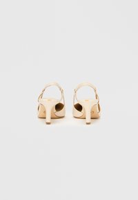 Beiget avokkaat, joissa on avoin kantapää, ohuet remmit ja sileä nahkapinta. Kengissä on siro korko ja minimalistinen muotoilu.