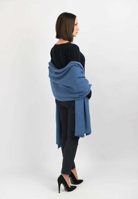 Blå stofsjawl draperet over en sort sweater med en blød tekstur. Sorte tætsiddende bukser og spidse højhælede sko fuldender looket.