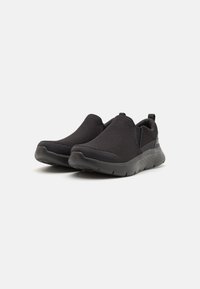 Zapatos negros de tipo slip-on con parte superior de malla texturizada, cuello acolchado y suela acolchada para mayor comodidad y flexibilidad.