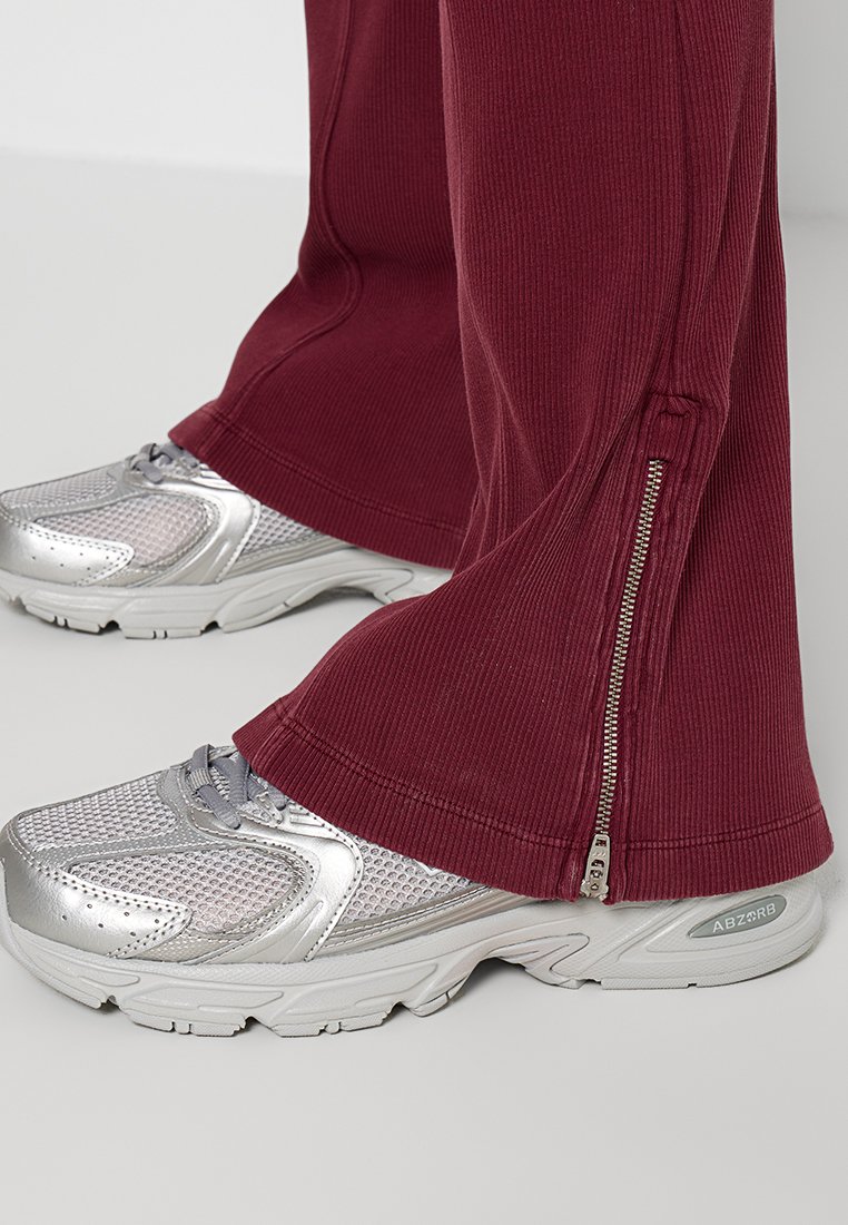 Maroon geribbelde sportbroeken met ritsen aan de zoom, gecombineerd met zilveren mesh hardloopschoenen met een gestructureerde bovenkant en een gevoerde zool.