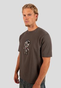 Tmavě šedé bavlněné tričko s texturovanou grafikou medvědí postavy s jemnými vzory a červeným akcentem srdce na přední straně.