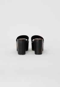 Black platform clogs with a smooth texture, rounded back, and wide straps. The chunky block heel is integrated into the sole design.