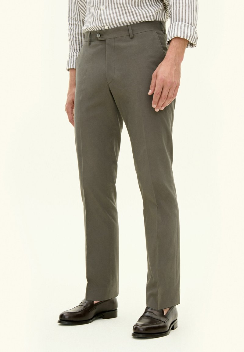 Pantaloni verde oliva su misura, realizzati in tessuto leggero, con una texture liscia e una vestibilità slim, abbinati a mocassini marrone scuro.