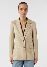 Beiger gestreifter Blazer mit Reverskragen, zwei Fronttaschen und zwei Knöpfen. Akzentuiert durch schmale weiße Streifen und eine strukturierte Passform.