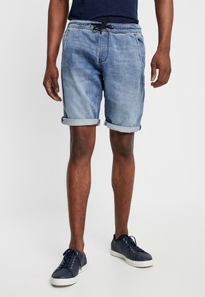 Shorts en denim bleu clair avec revers, dotés d'une taille élastique et d'un cordon de serrage. Associés à des baskets bleu foncé.