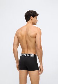 Svarta bomullsboxer med en kontrasterande vit midjeband som har "CALVIN KLEIN"-logotypen. Slät textur och åtsittande design.